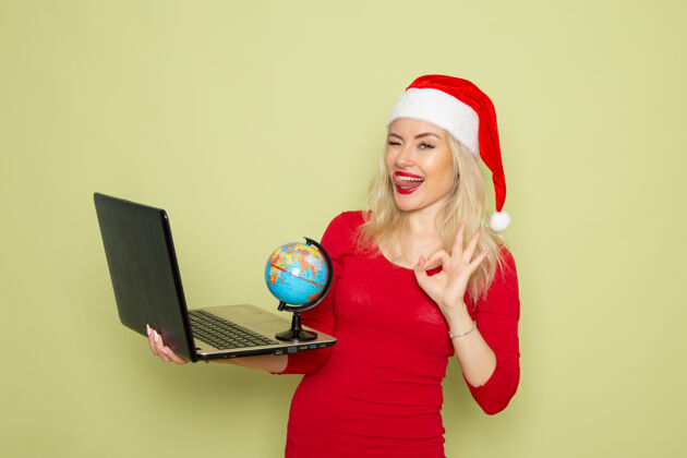 磁盘骑师正面图漂亮的女人拿着地球仪和笔记本电脑在绿色的墙上度假情绪圣诞雪新年的颜色漂亮的女性成人地球仪