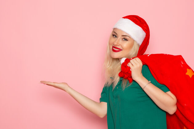 肖像正面图年轻女性拎着红包带着礼物在粉色墙上度假模特圣诞新年彩照美丽圣诞微笑