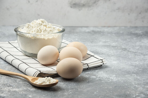 奶制品一碗面粉和生鸡蛋放在桌布上玻璃面粉碗