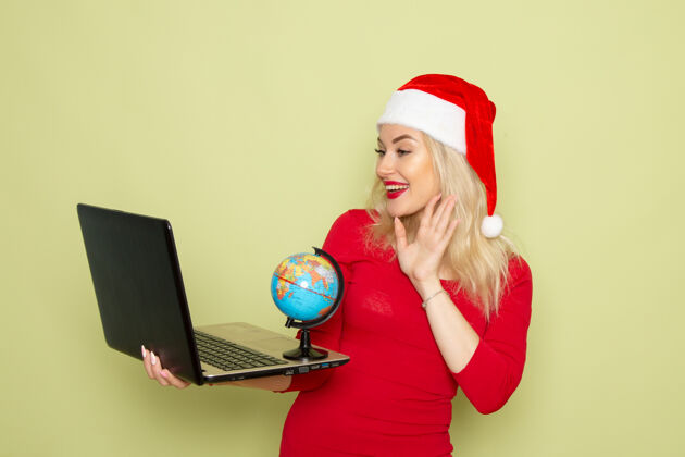 漂亮的女性正面图漂亮的女人拿着地球仪 用笔记本电脑在绿墙上过节感慨圣诞雪新年的颜色地球仪情绪漂亮