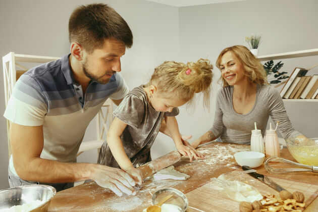 晚餐可爱的小女孩和她美丽的父母在家里的厨房里为蛋糕准备面团午餐吃饭烹饪