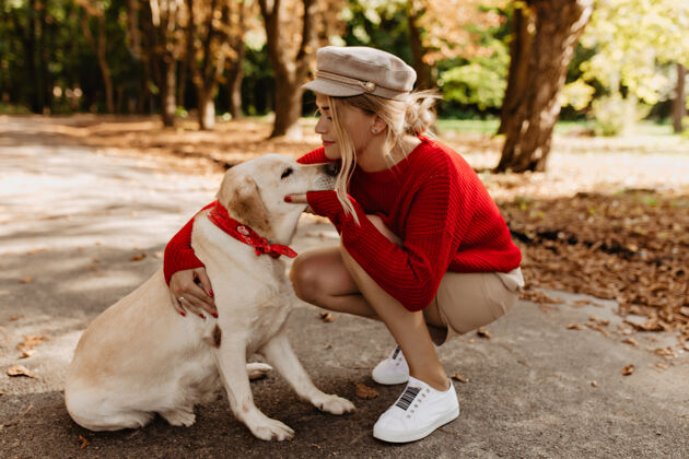 女人迷人的金发女郎和可爱的拉布拉多一起在秋天的公园度过一天穿着季节性服装的女孩拥抱她心爱的狗的动人照片年轻快乐家养