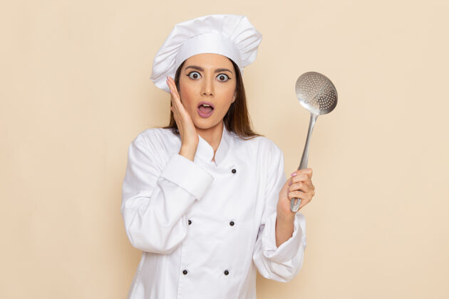 人身穿白色厨师服的年轻女厨师正拿着大银勺站在浅白的墙上烹饪工作专业