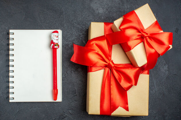 圣诞节上图为圣诞背景 带有蝴蝶结形缎带的精美礼物和深色背景上带笔的笔记本蝴蝶结笔记本钢笔