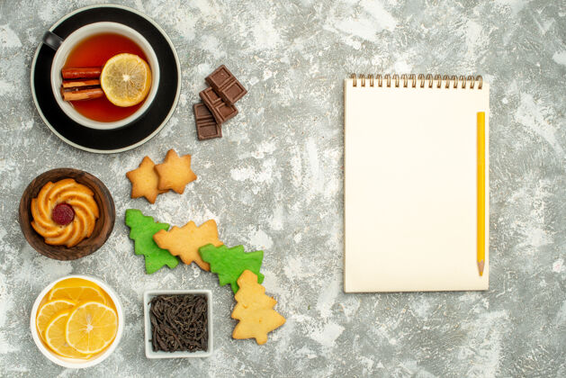 饼干顶视图圣诞树饼干茶碗杯巧克力和柠檬片笔记本铅笔在灰色的桌子上笔记本巧克力茶