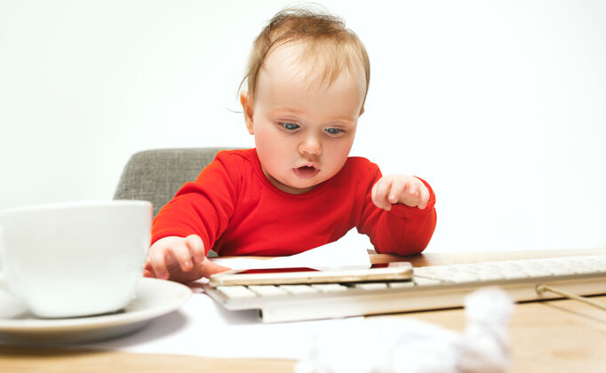 惊喜小女婴坐在白色工作室里 用现代电脑或笔记本电脑的键盘孩子惊喜科技