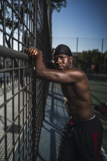形状一个半裸的非洲裔美国男子斜靠在篮球场的栅栏上的垂直镜头运动员健康瘦
