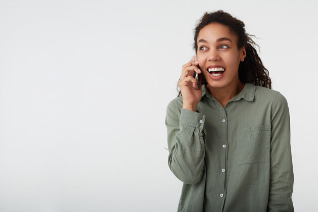 白色快乐的年轻迷人的卷发黑发黑皮肤的女士 在愉快的电话交谈时 举着手机 在白色背景下孤立女士情绪交谈