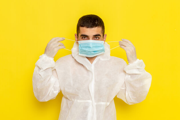 实验室身穿特殊防护服的男科学工作者戴着面具站在黄色墙上的正面图正面成人服装