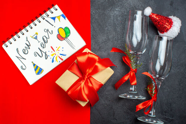 视图顶视图圣诞背景与圣诞老人帽子玻璃高脚杯笔记本与新年写作和图纸和礼物上的红色和黑色背景圣诞圣诞背景玻璃