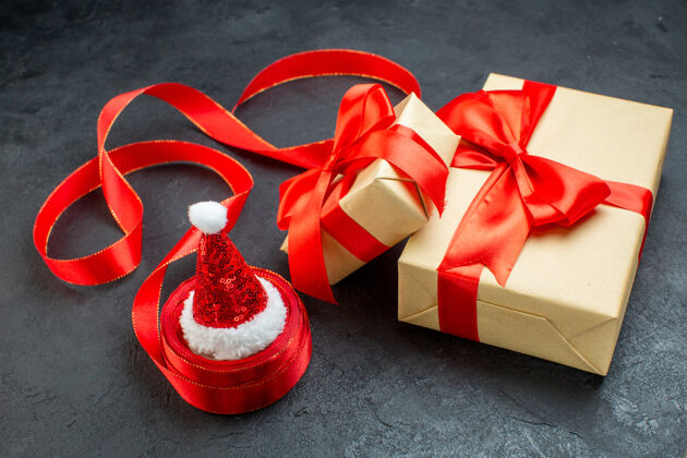 蝴蝶结在一张深色的桌子上 红色丝带和圣诞老人帽子的美丽礼物的正面视图惊喜帽子圣诞老人