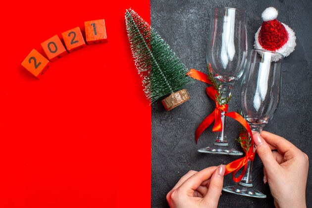 玻璃高脚杯手持玻璃高脚杯的顶视图 红色和黑色背景上的圣诞树数字圣诞老人帽帽子手工工具设备
