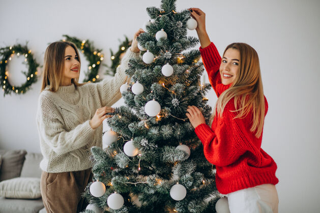 庆祝两个女孩在装饰圣诞树红毛衣女孩乐趣