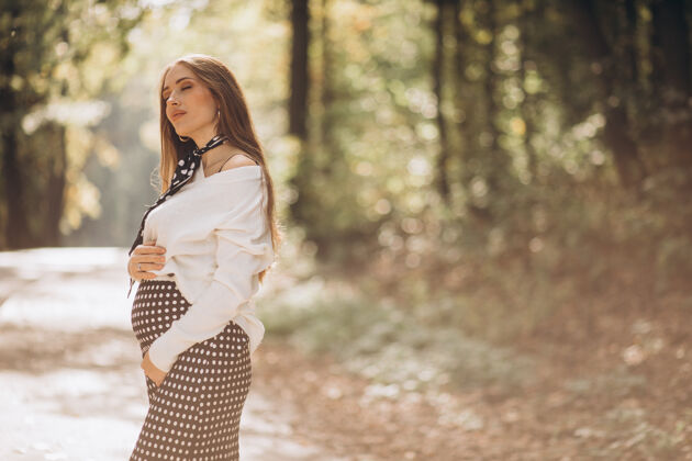 快乐美丽的孕妇在秋天的公园里帽子腹部公园