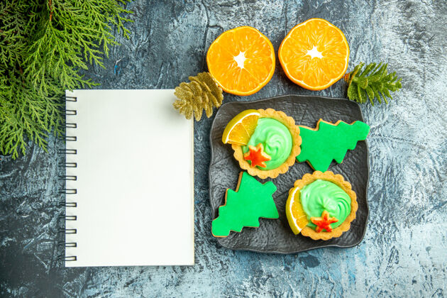 糖果俯视图小馅饼圣诞树饼干在黑色盘子上切橘子笔记本在灰色桌子上盘子树饼干