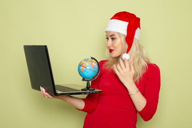 小正面图漂亮的女人拿着地球仪和笔记本电脑在绿色的墙上圣诞节颜色雪节日新年的情绪漂亮肖像成人