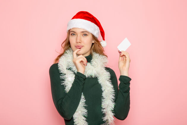 情绪正面图年轻女性手持白色银行卡在粉色墙壁上的彩色情感模型假日圣诞新年圣诞节看法漂亮