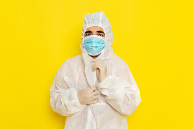 正面身穿特殊防护服的男科学工作者戴着面具站在黄色墙上的正面图科学实验室服装
