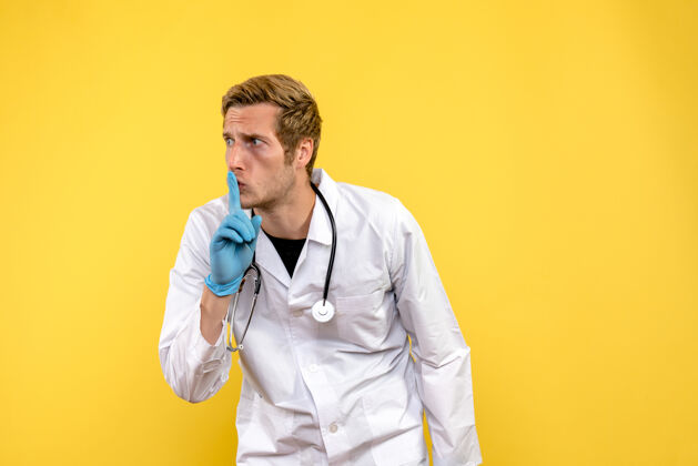 肖像正面图黄色背景上男医生要求安静健康人病毒医生视图听诊器专业