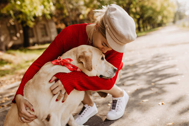 漂亮漂亮的女孩戴着时髦的帽子 穿着白色运动鞋 温柔地抱着她的狗可爱的金发女郎和她的宠物坐在公园里青少年朋友狗