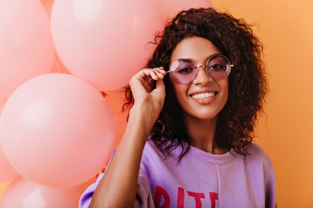 女人迷人的生日女孩在拍照时触摸她的眼镜时尚的非洲女人拿着粉色的派对气球可爱庆典节日