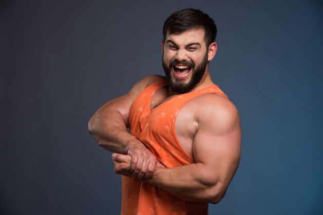 强壮运动员在深蓝色的墙上展示他的肌肉沉重男人肌肉