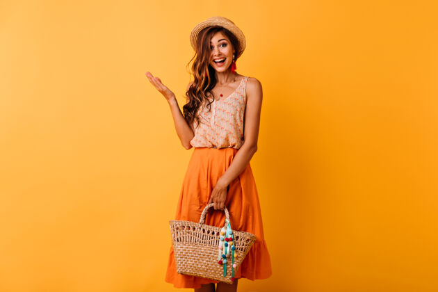波西米亚兴奋的姜女士戴着帽子拿着草包欣喜若狂的长发女孩穿着夏装享受美好的一天橙色裙子乐趣