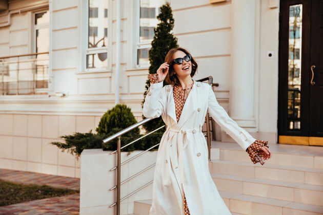 城市穿着白色长外套的兴奋的女模特正在享受美好的一天穿着秋装的活跃的年轻女子的户外镜头乐趣户外户外