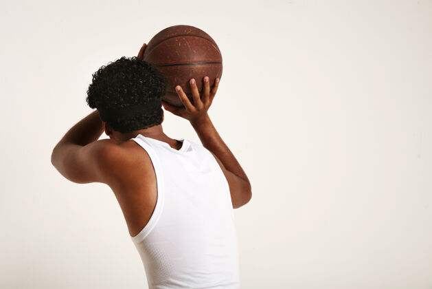 运动员肌肉发达 皮肤黝黑 头戴非洲裔头带 身穿白色无袖衬衫的运动员 将一个棕色的旧皮球扔在白色的衣服上年轻人非洲专业
