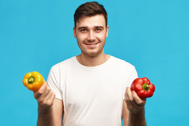 铃铛人 有机食品 营养 素食和健康的生活方式的概念肖像英俊积极的年轻男性穿着白色t恤手持红黄色的甜椒 去做沙拉男士切割胡椒
