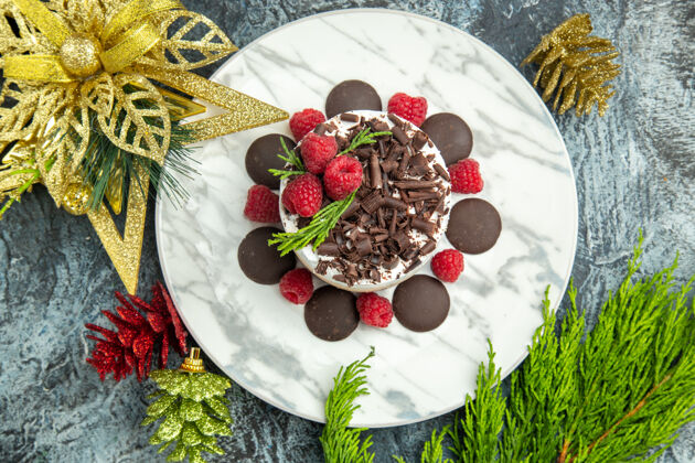 浆果顶视芝士蛋糕与巧克力和覆盆子在白色椭圆形板圣诞饰品在灰色表面椭圆形视图顶部