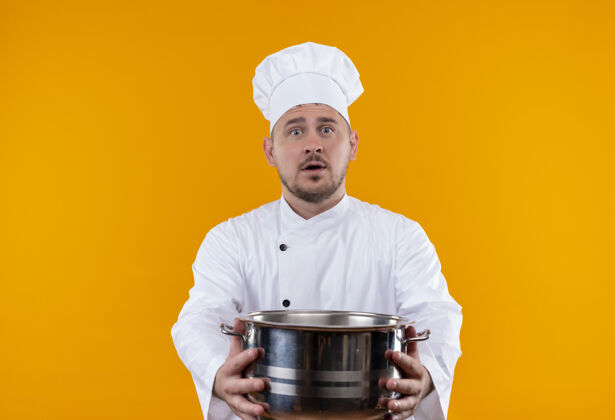 厨师穿着厨师制服的年轻帅哥厨师在孤立的橙色空间里伸出锅炉年轻帅哥伸展