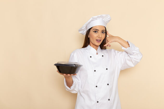 女身穿白色厨师服的年轻女厨师手持黑色平底锅站在白色墙壁上的正视图饭举行烹饪