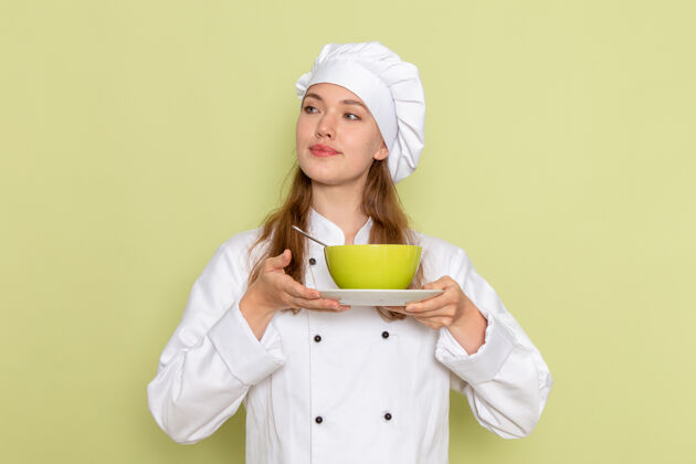 人身穿白色厨师服的女厨师正拿着绿色盘子 绿色墙壁上有盘子食物饭烹饪