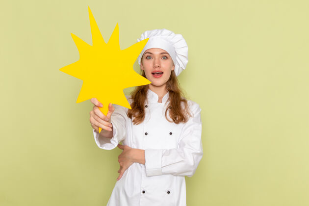 举行女厨师身穿白色厨师服 手持绿色墙壁上的黄色标志 正视图专业女性穿着