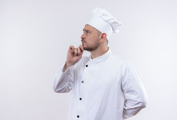 放体贴的年轻帅哥厨师身着厨师制服 手放在下巴上 站在侧视图中 看着隔离在空白处的一侧厨师帅气厨师