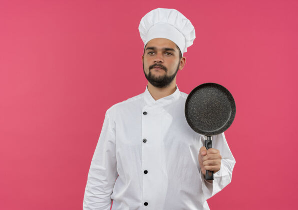 平底锅身穿厨师制服的年轻男厨师手拿煎锅 在粉红色的空间里看起来很孤独复制厨师直