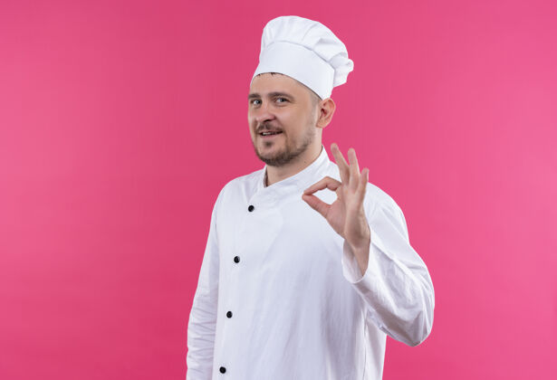 招牌面带微笑的年轻帅哥厨师身着厨师制服 在粉色空间上做着“ok”标志帅气厨师微笑