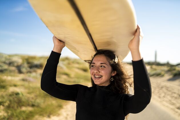 携带特写镜头中一个微笑的女性头上举着冲浪板爱好海滩美丽