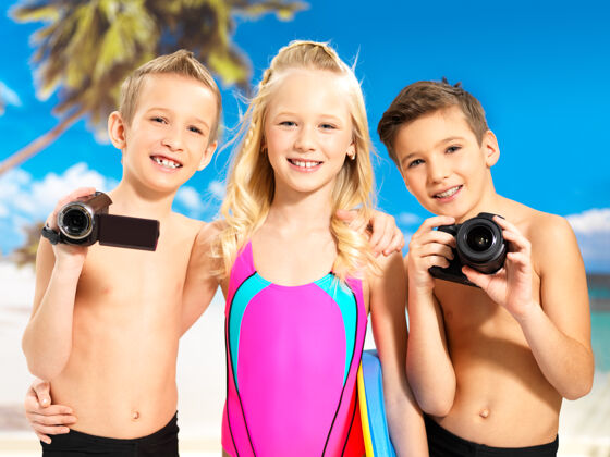 阳光快乐的孩子们在海滩上玩耍的画像小学生手里拿着照片和摄像机站着乐趣颜色海岸