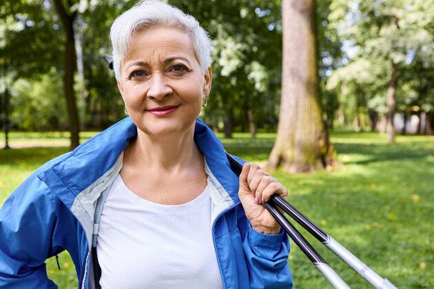 活跃夏季 运动 娱乐 健康和活动的概念户外拍摄的迷人的精力旺盛的老妇人在蓝色夹克摆姿势在森林与棒北欧散步老年人北欧草地