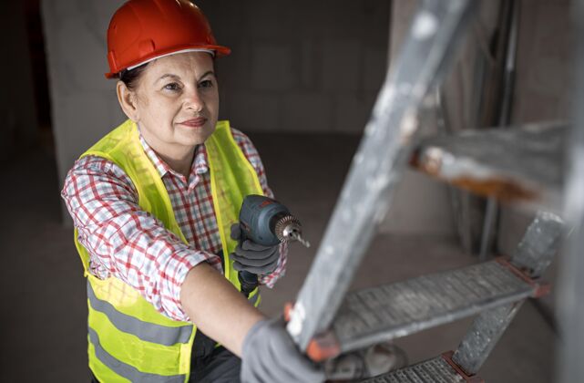 工作高角度的女建筑工人用电钻帽子妇女背心