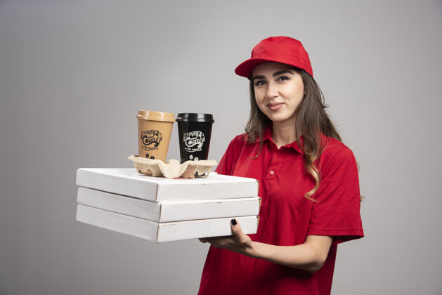 制服送披萨和咖啡杯的女人站在灰色的墙上餐食员工工作