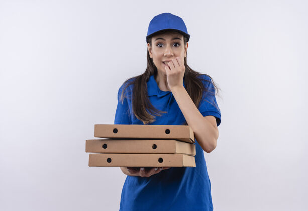 站着穿着蓝色制服 戴着帽子 手里拿着一叠披萨盒的年轻送货女孩紧张得咬指甲制服年轻送货