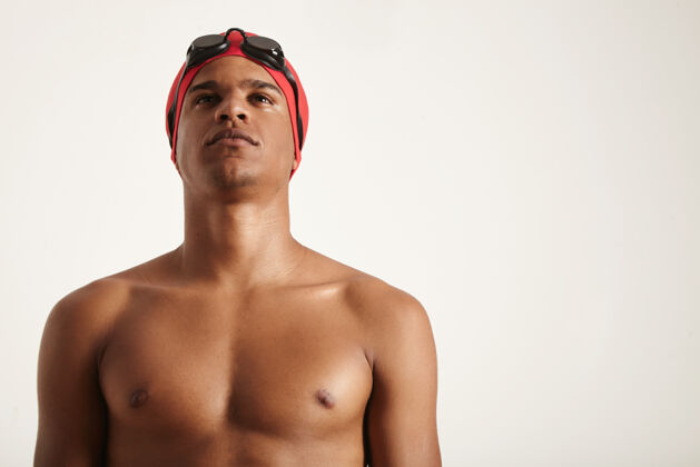 肌肉年轻坚定的非洲裔美国游泳运动员戴着红色的帽子和黑色的护目镜仰望白色追求帽子健身