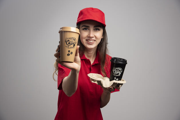 承运人穿着红色制服的女送货员在展示咖啡杯工作杯子微笑