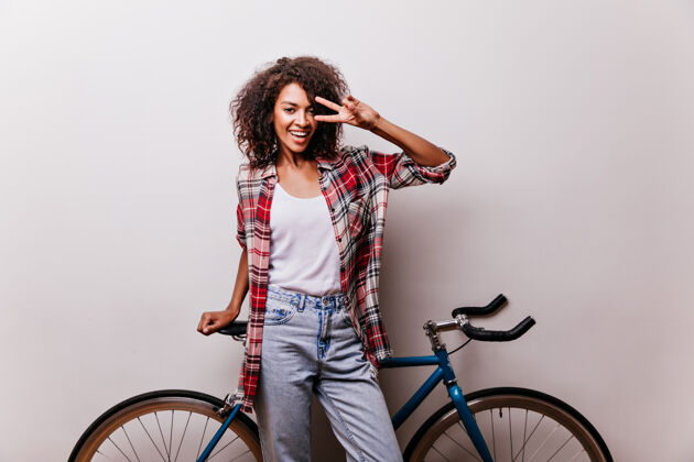 苗条穿着格子衬衫的迷人的女自行车手在笑幽默的女人与自行车合影 表达幸福可爱卷发人
