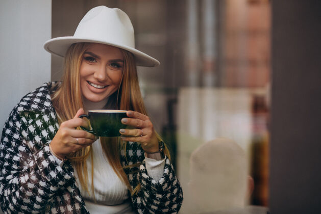 杯子在咖啡馆喝咖啡的女人 坐在玻璃后面白天休闲在玻璃后面