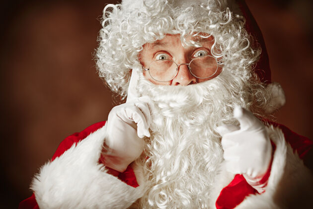节日穿着圣诞老人服装 留着奢华的白胡子 戴着圣诞老人的帽子 穿着红色服装的惊讶男人的肖像传统的胡须圣人