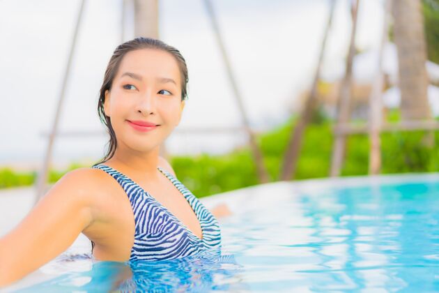 治疗肖像美丽的亚洲年轻女子放松休闲周围的室外游泳池与海洋海滩阳光年轻人蓝色